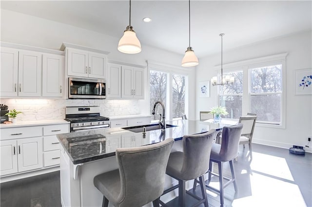 kitchen with sink, decorative light fixtures, stainless steel appliances, a kitchen island with sink, and white cabinets