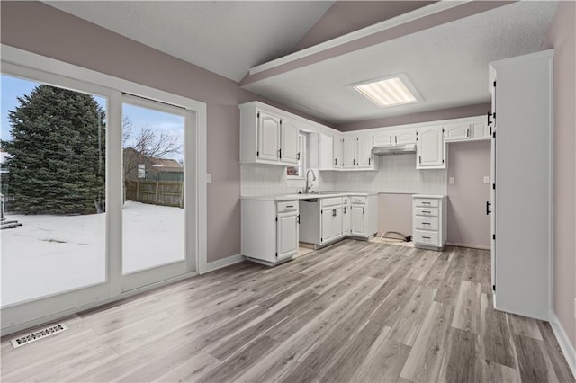 kitchen with white cabinets, lofted ceiling, light wood-type flooring, stainless steel dishwasher, and decorative backsplash