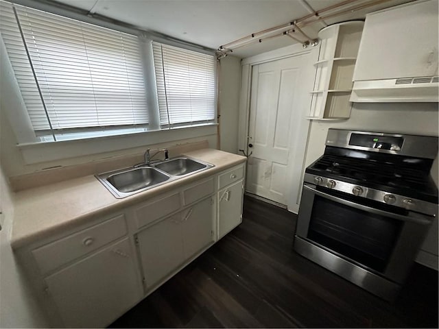 kitchen with stainless steel gas range oven, dark wood-type flooring, sink, white cabinets, and range hood