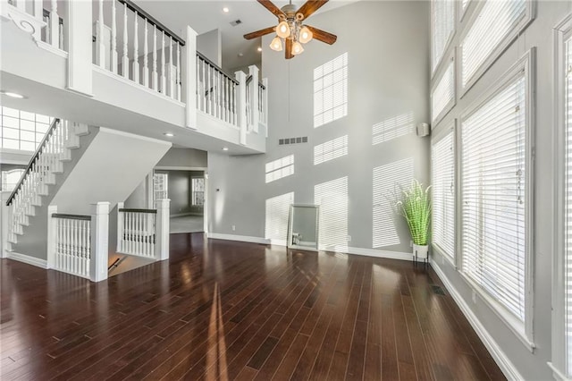 unfurnished living room with a high ceiling, dark wood-type flooring, and ceiling fan