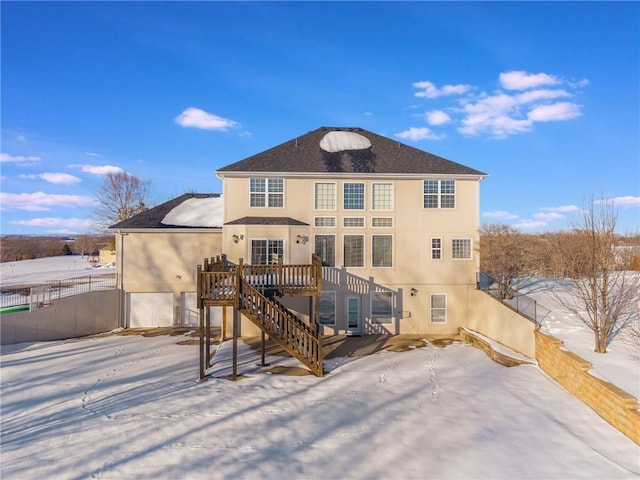 snow covered rear of property with a deck and a garage