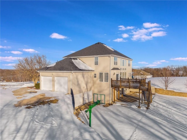 snow covered rear of property featuring a deck and a garage