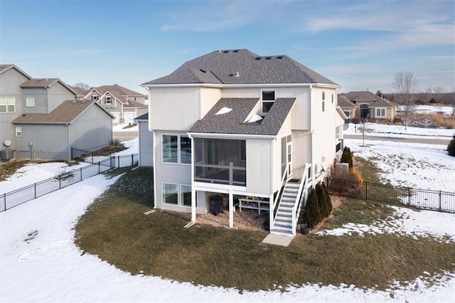 snow covered back of property featuring a sunroom, a lawn, and central AC