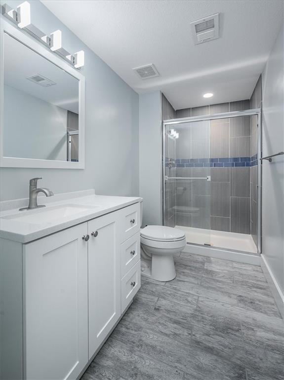 bathroom with a shower with shower door, toilet, and vanity