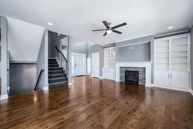 unfurnished living room featuring ceiling fan, a tile fireplace, crown molding, dark wood-type flooring, and built in features