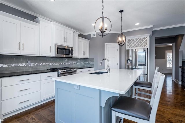 kitchen with appliances with stainless steel finishes, a center island with sink, hanging light fixtures, and sink