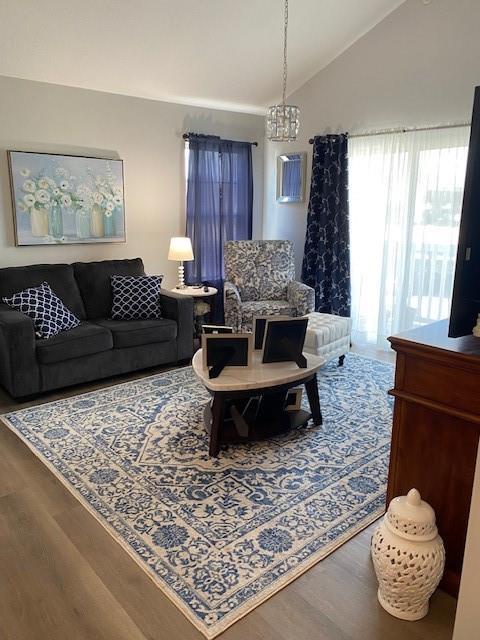 living room featuring an inviting chandelier, vaulted ceiling, and hardwood / wood-style flooring