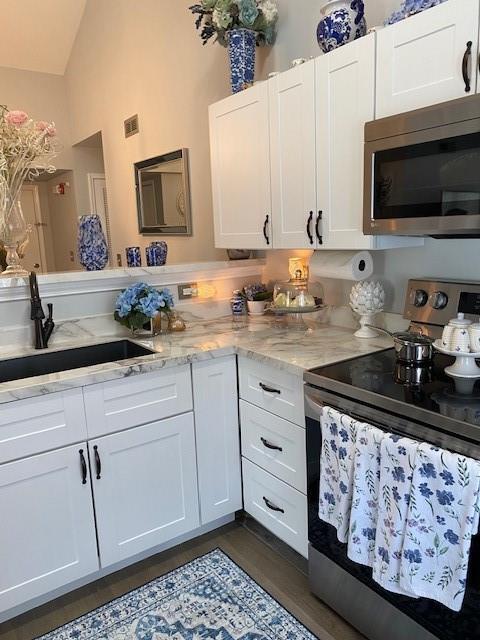 kitchen with light stone countertops, sink, stainless steel appliances, vaulted ceiling, and white cabinets