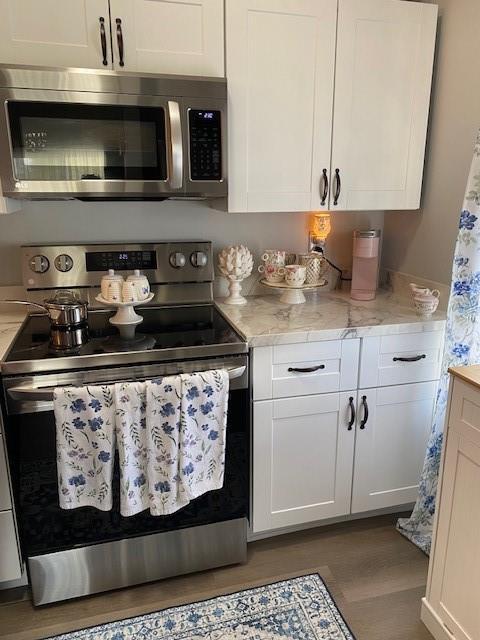 bar featuring light stone counters, white cabinets, dark hardwood / wood-style floors, and appliances with stainless steel finishes