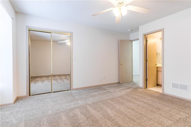 unfurnished bedroom featuring ensuite bath, light carpet, ceiling fan, and a closet