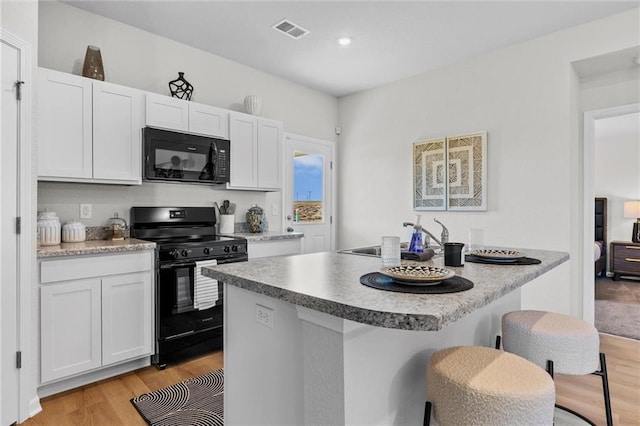 kitchen with black appliances, white cabinets, a kitchen breakfast bar, and light hardwood / wood-style floors