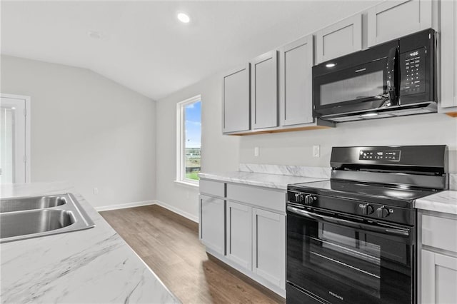 kitchen with dark hardwood / wood-style floors, lofted ceiling, light stone countertops, black appliances, and sink