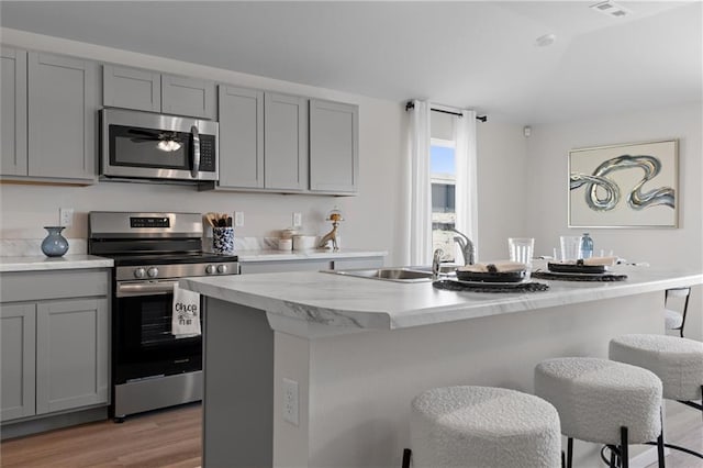 37767 W 207th Ter, Edgerton, KS 66021 - kitchen with stainless steel appliances, gray cabinetry, light wood-type flooring, a kitchen breakfast bar, and a center island with sink