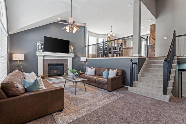 carpeted living room with ceiling fan with notable chandelier, a tile fireplace, and high vaulted ceiling