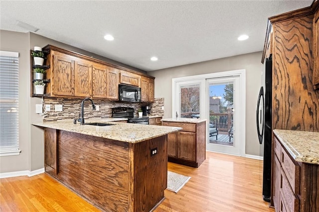 kitchen with light stone counters, sink, black appliances, and kitchen peninsula