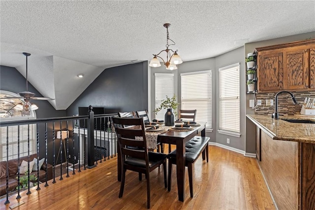 dining area with ceiling fan with notable chandelier, a textured ceiling, sink, vaulted ceiling, and light hardwood / wood-style flooring