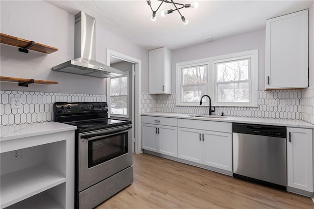 kitchen with sink, wall chimney exhaust hood, appliances with stainless steel finishes, white cabinets, and light wood-type flooring