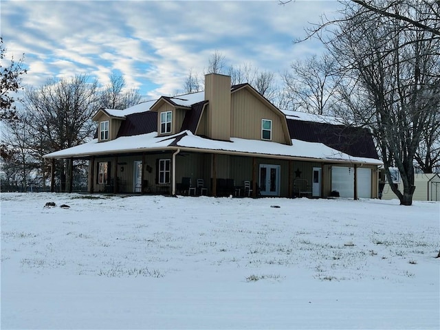 snow covered rear of property with covered porch and a garage