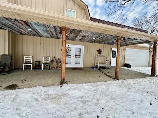 snow covered patio featuring a garage and french doors