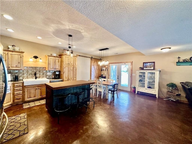 kitchen with a barn door, backsplash, wooden counters, sink, and hanging light fixtures