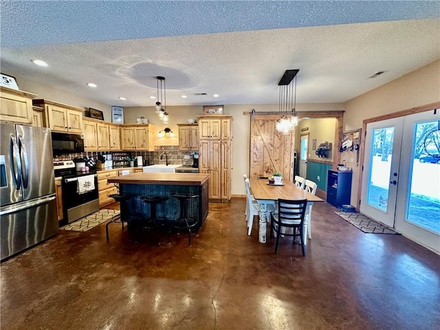 kitchen featuring hanging light fixtures, a barn door, a kitchen island with sink, and appliances with stainless steel finishes