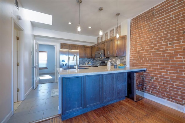 kitchen with pendant lighting, sink, stainless steel appliances, brick wall, and kitchen peninsula