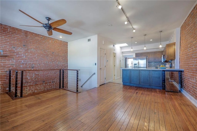 kitchen featuring stainless steel refrigerator with ice dispenser, decorative light fixtures, kitchen peninsula, brick wall, and light hardwood / wood-style floors