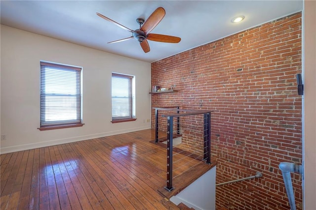 unfurnished living room with wood-type flooring, ceiling fan, and brick wall