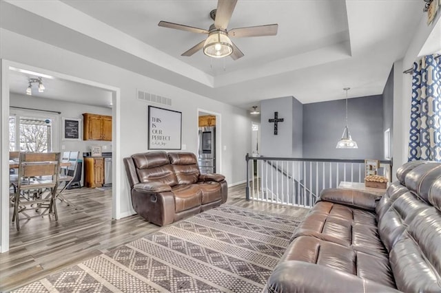 living room featuring ceiling fan, light hardwood / wood-style floors, and a raised ceiling