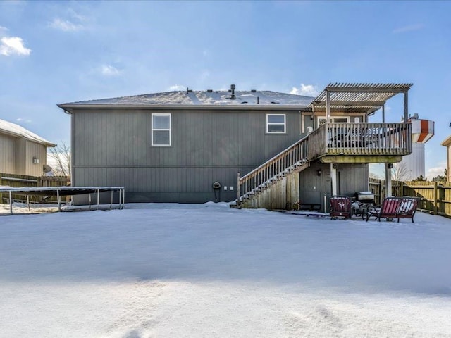 snow covered back of property with a wooden deck, a pergola, and a trampoline