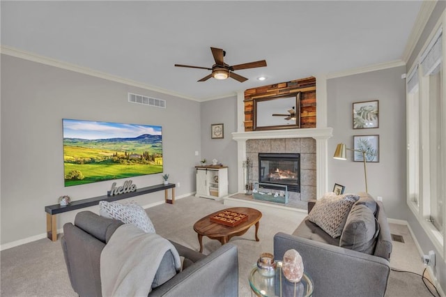 carpeted living room with ornamental molding, ceiling fan, a wealth of natural light, and a tiled fireplace