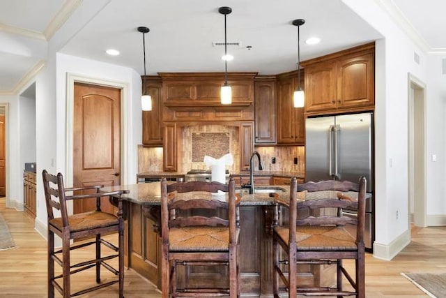 kitchen featuring a center island with sink, a kitchen bar, hanging light fixtures, and high end refrigerator