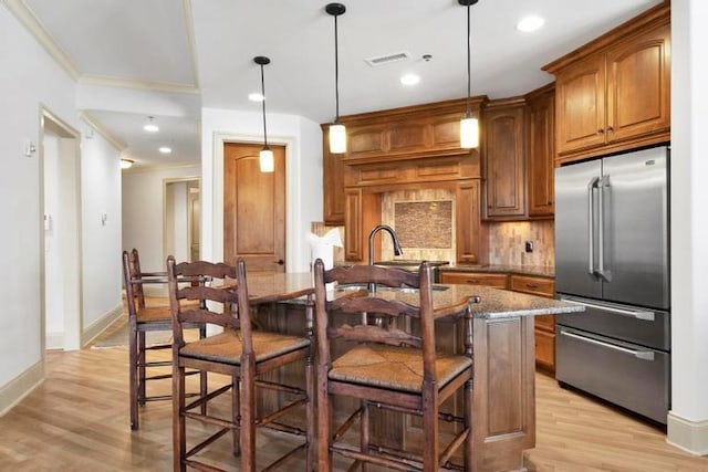 kitchen featuring dark stone countertops, pendant lighting, a breakfast bar area, high quality fridge, and a center island with sink