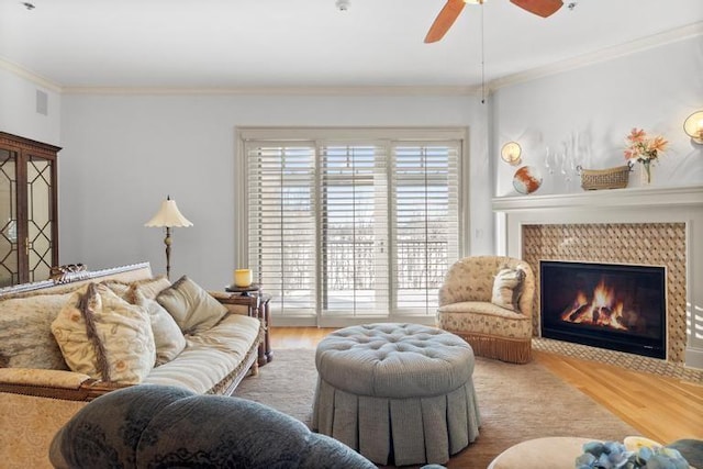 living room featuring hardwood / wood-style floors, ceiling fan, crown molding, and a tile fireplace