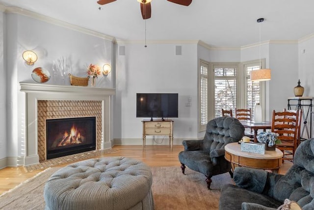 living room featuring a tile fireplace, crown molding, ceiling fan, and wood-type flooring