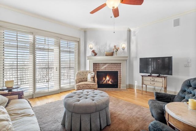 living room with light hardwood / wood-style floors, a brick fireplace, ceiling fan, and crown molding