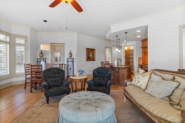 living room featuring light hardwood / wood-style floors, ceiling fan, ornamental molding, and sink