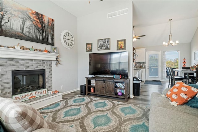 living room featuring ceiling fan with notable chandelier, dark hardwood / wood-style floors, a brick fireplace, and lofted ceiling