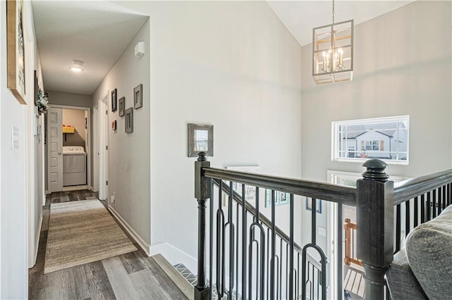 hallway featuring hardwood / wood-style flooring, washer / dryer, lofted ceiling, and an inviting chandelier