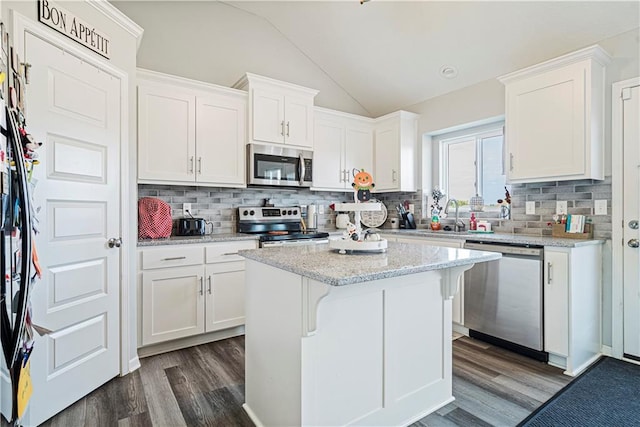 kitchen with light stone countertops, white cabinetry, stainless steel appliances, vaulted ceiling, and a kitchen island