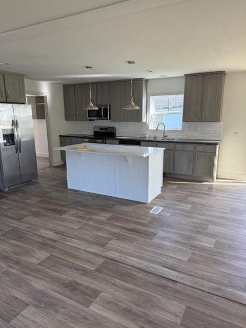 kitchen featuring wood-type flooring, appliances with stainless steel finishes, a kitchen island, sink, and decorative light fixtures