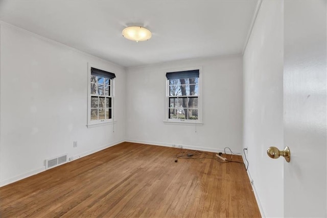 spare room featuring visible vents, crown molding, baseboards, and wood finished floors