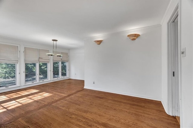 empty room with baseboards, wood finished floors, and crown molding