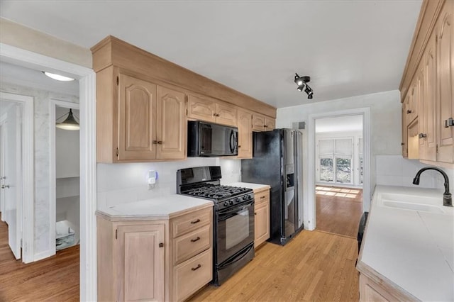 kitchen with light wood-style flooring, light brown cabinets, black appliances, and a sink