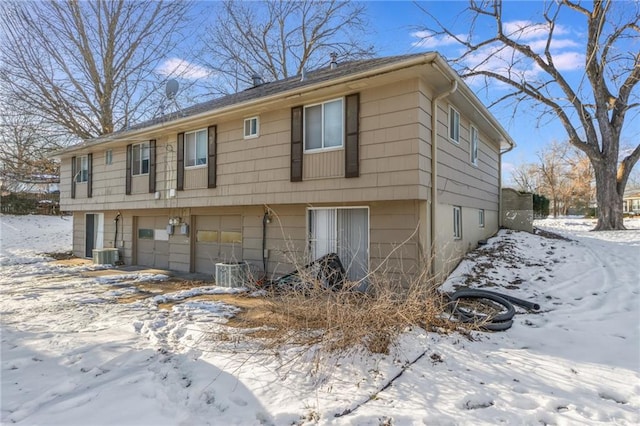 snow covered back of property featuring a garage and central air condition unit