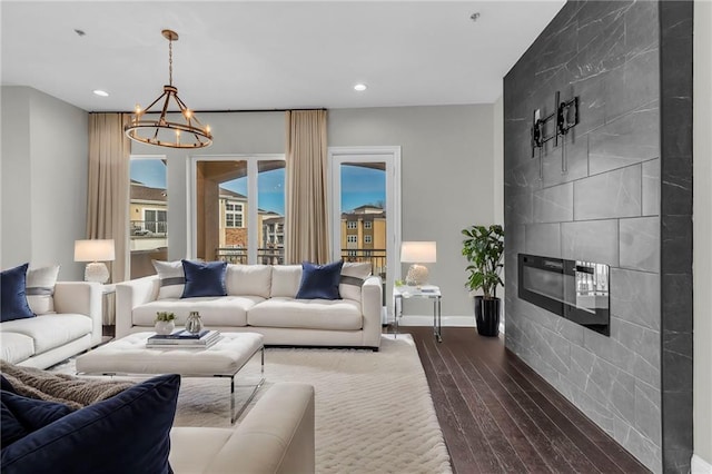 living room featuring dark hardwood / wood-style floors, a tiled fireplace, and an inviting chandelier