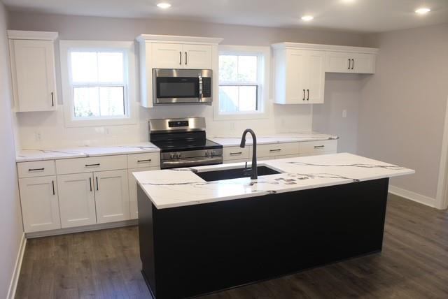 kitchen with light stone countertops, white cabinetry, stainless steel appliances, dark hardwood / wood-style floors, and a center island with sink