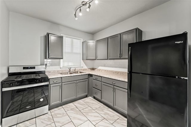 kitchen featuring gray cabinets, decorative backsplash, sink, black refrigerator, and gas range