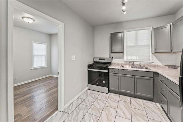 kitchen with gray cabinets, gas stove, tasteful backsplash, and sink