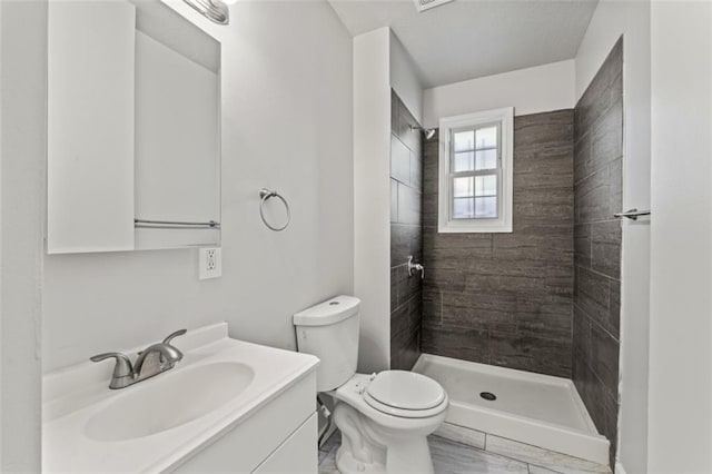 bathroom with toilet, a tile shower, and vanity